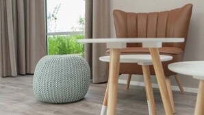 Een moderne woonkamer met een bruine leren fauteuil, een rond hocker en een witte tafel met houten poten.