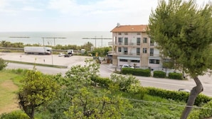 Un immeuble à plusieurs étages doté d’un balcon, situé près d’une route et d’un plan d’eau.