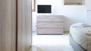 Une chambre moderne avec une armoire en bois, une table de chevet, un lit avec une couette, un téléviseur à écran plat et un grand miroir au mur.
