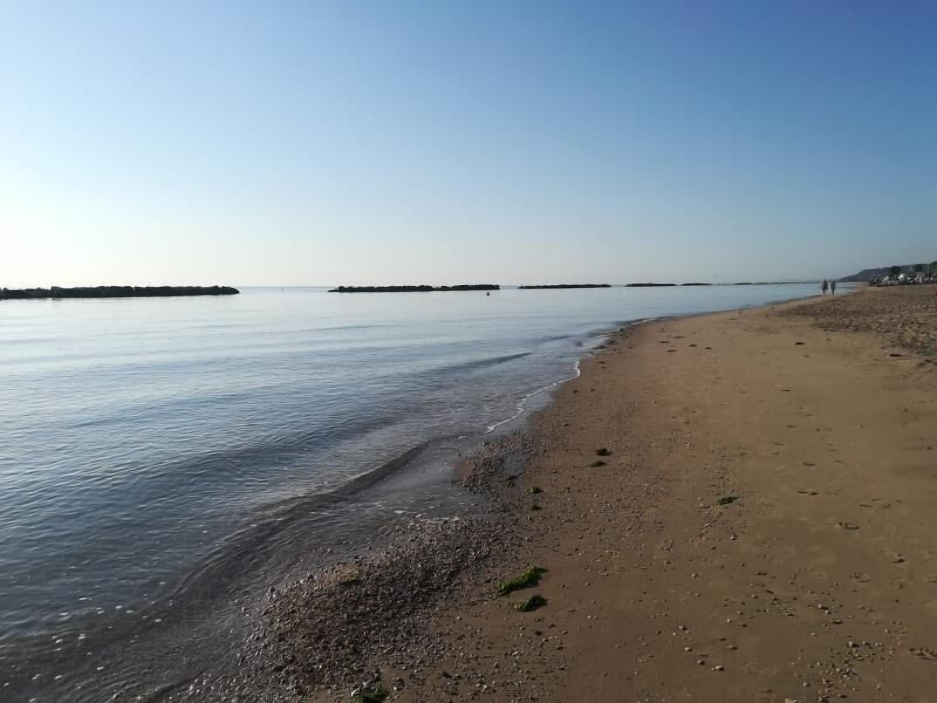 A beach with calm water, a sandy shore, and distant landforms.