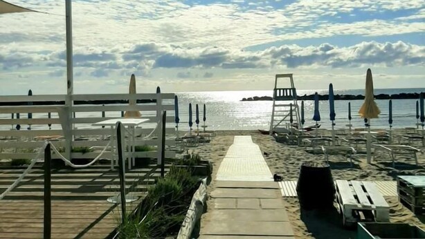 Une plage avec une promenade en bois menant à l’eau, des chaises longues, des parasols et une vue dégagée sur la mer.