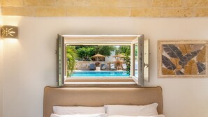 Ett hotellrum med en säng, ett fönster med fri utsikt över en pool och en utomhusplats, samt en dekorativ väggdekoration.