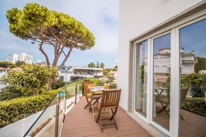Un balcón con mesa y sillas, con vistas a un jardín y un paisaje urbano.