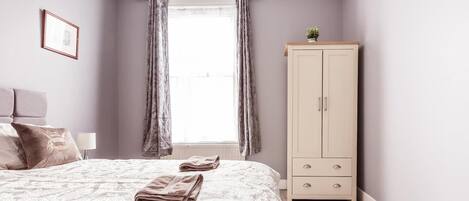 Un dormitorio con cama, armario, ventana con cortinas y un cuadro en la pared.