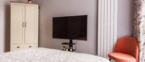 A bedroom with a bed, a television, a wardrobe, and a chair.