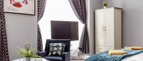 Una habitación de hotel moderna con cama, escritorio, silla, armario y un gran ventanal con cortinas.