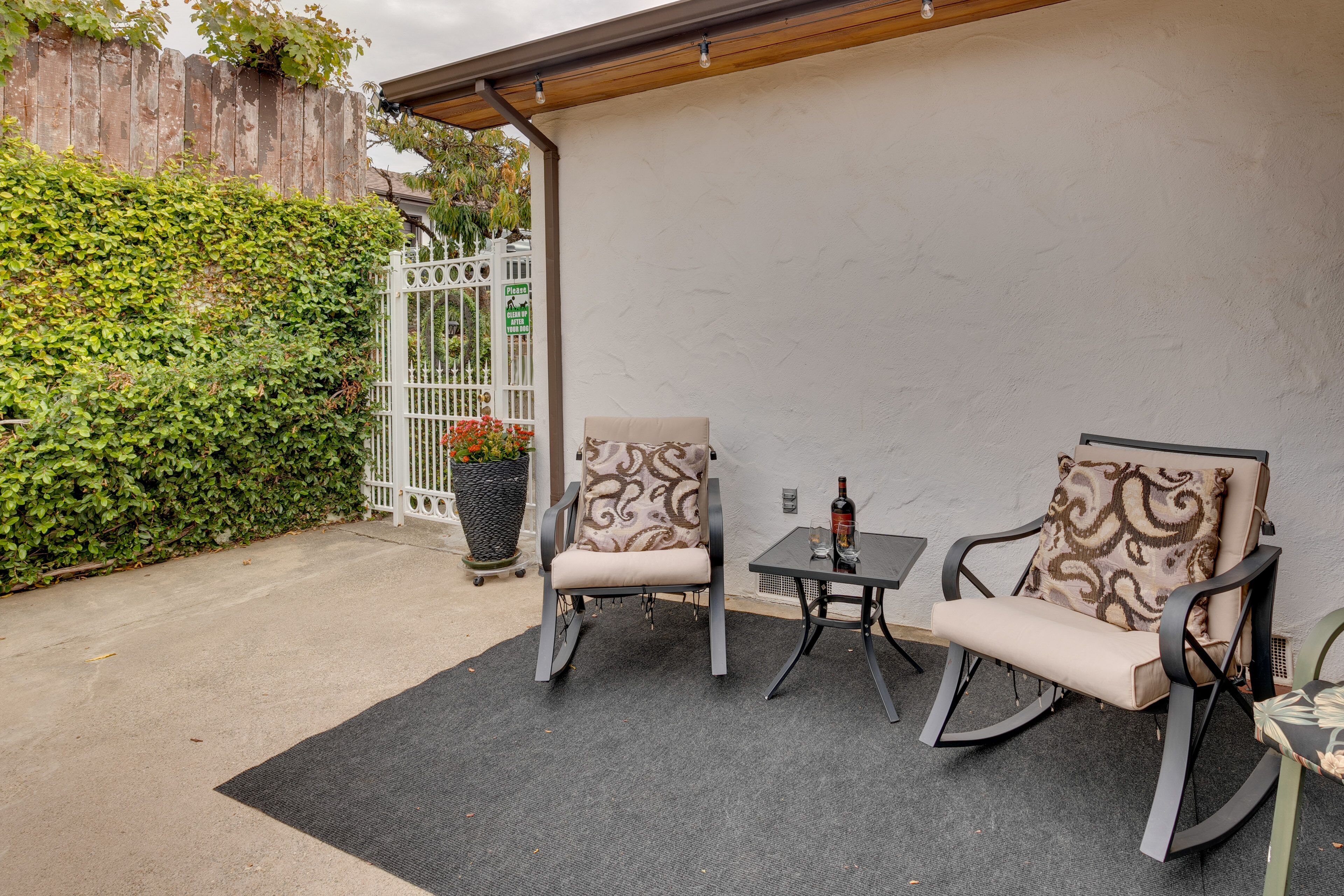 An outdoor patio area with two rocking chairs and a small table, surrounded by a white wall and a wooden fence.