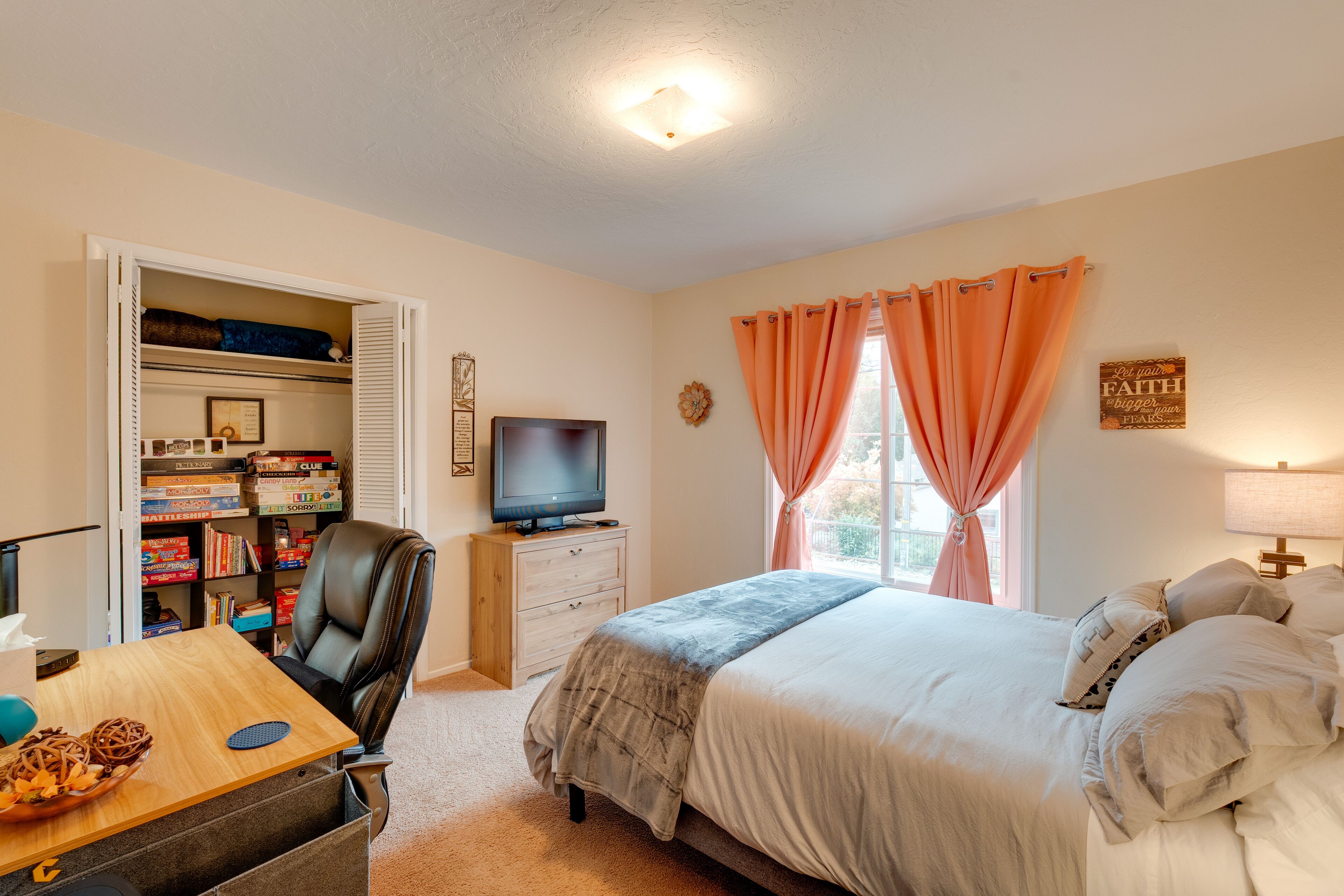 A bedroom with a bed, a desk with a computer, a chair, a television, and a closet with shelves.