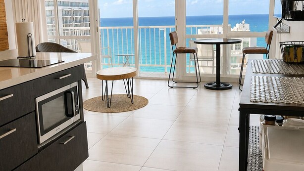 Een moderne keuken met een groot eiland, een eetgedeelte met uitzicht op zee en een balkon met uitzicht op de skyline van de stad.