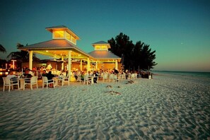 A beachside restaurant with outdoor seating and a covered area, overlooking the ocean.