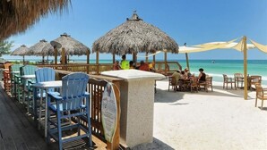 A beachside restaurant with thatched umbrellas, wooden tables, and chairs. - Bay & Gulf Views. Waterfront+heated quiet pool+AC+2-minute walk to beach (Bradenton Beach)