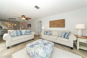 A modern living room with two sofas, a coffee table, and a ceiling fan.