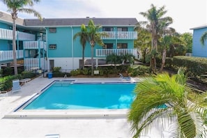 A pool area with a clear blue pool, surrounded by a two-story building with balconies.