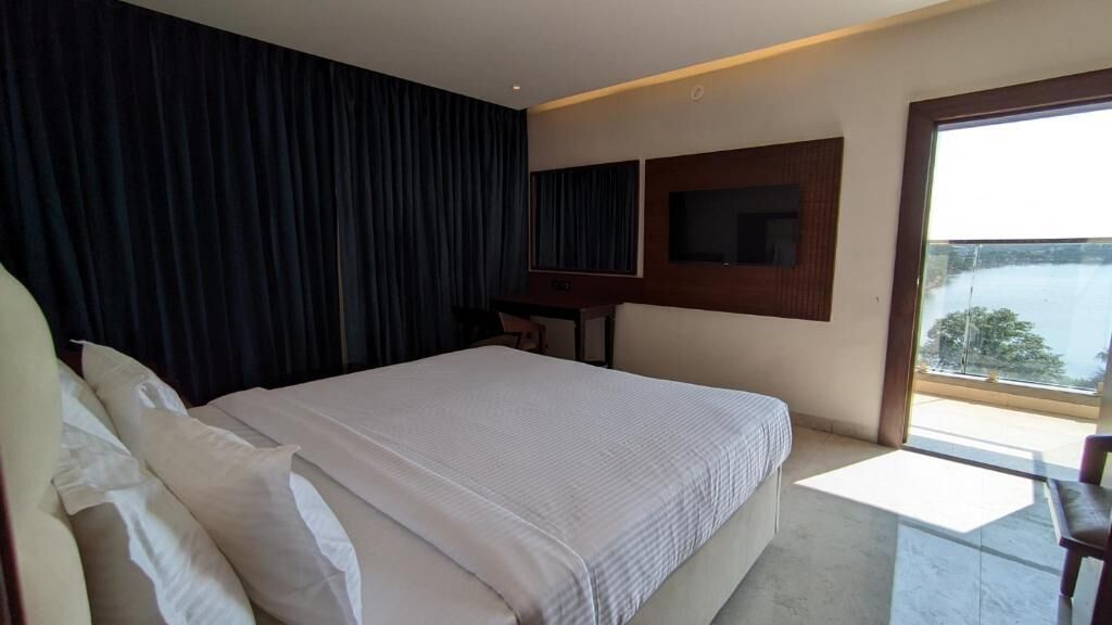 A hotel room with a large bed, a desk, a chair, a TV, and a balcony with a view.