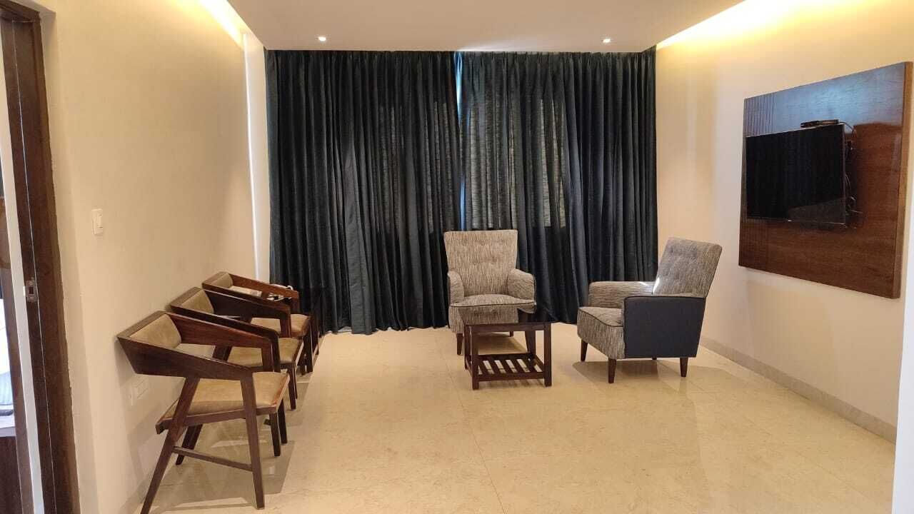 Una sala de estar con un ventanal grande, un televisor de pantalla plana montado en la pared y un conjunto de sillas de madera.