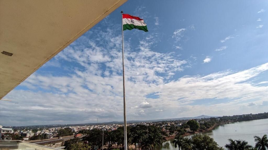 A flag on a pole, a body of water, and a distant cityscape.