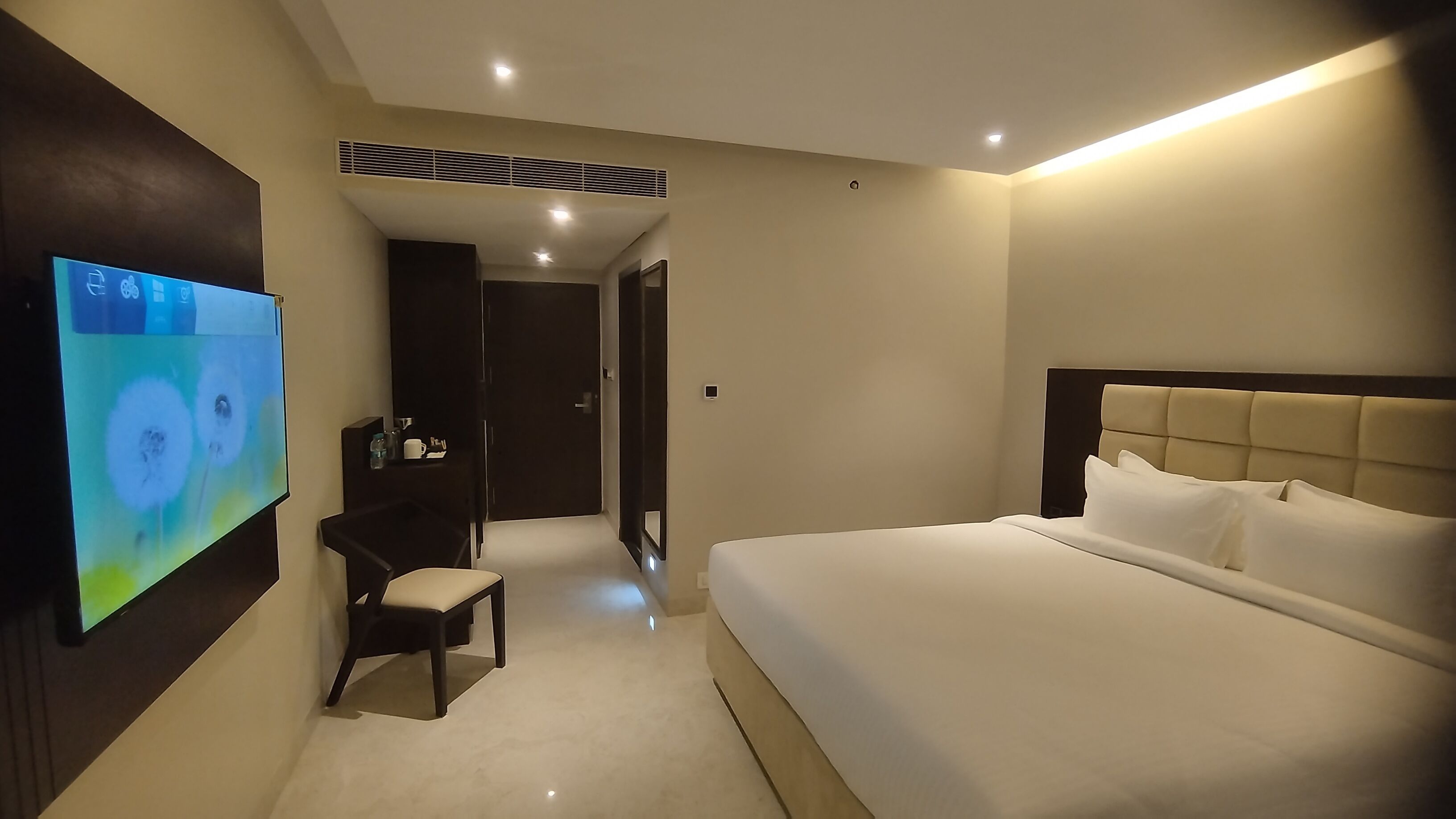 A modern hotel room with a large bed, a desk with a chair, a flat-screen TV, and a walk-in closet.