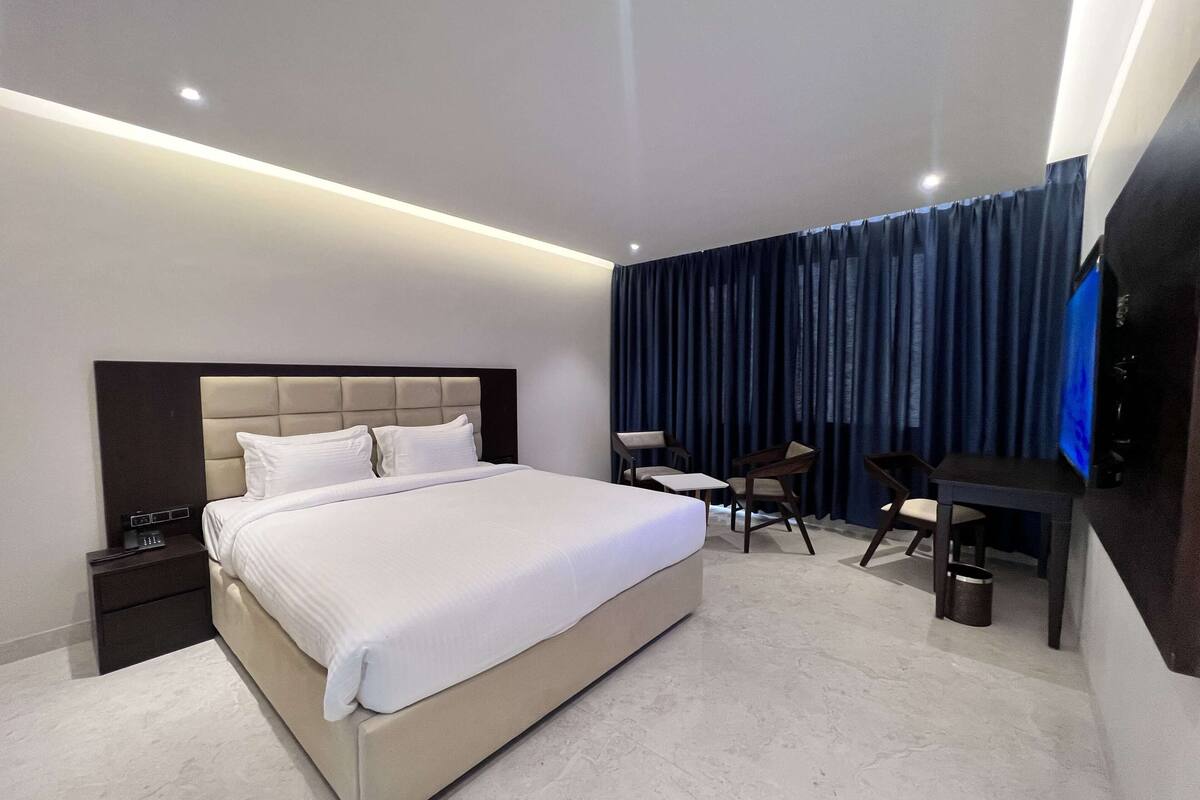 Ein modernes Hotelzimmer mit einem großen Bett, Nachttischen, einem Schreibtisch und einem Fernseher.