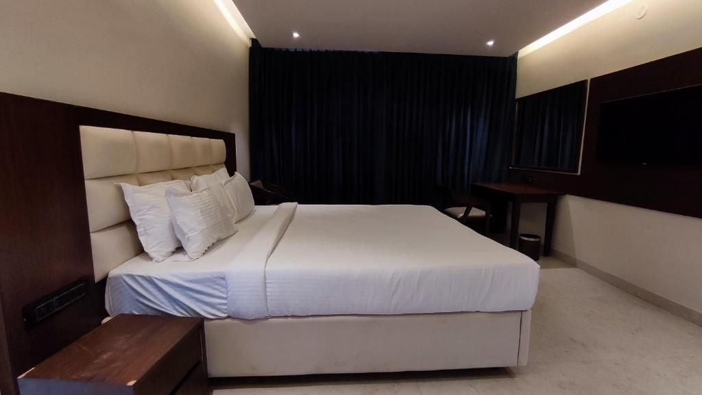 A modern hotel room with a large bed, a bedside table, a TV mounted on the wall, and a dark curtain.