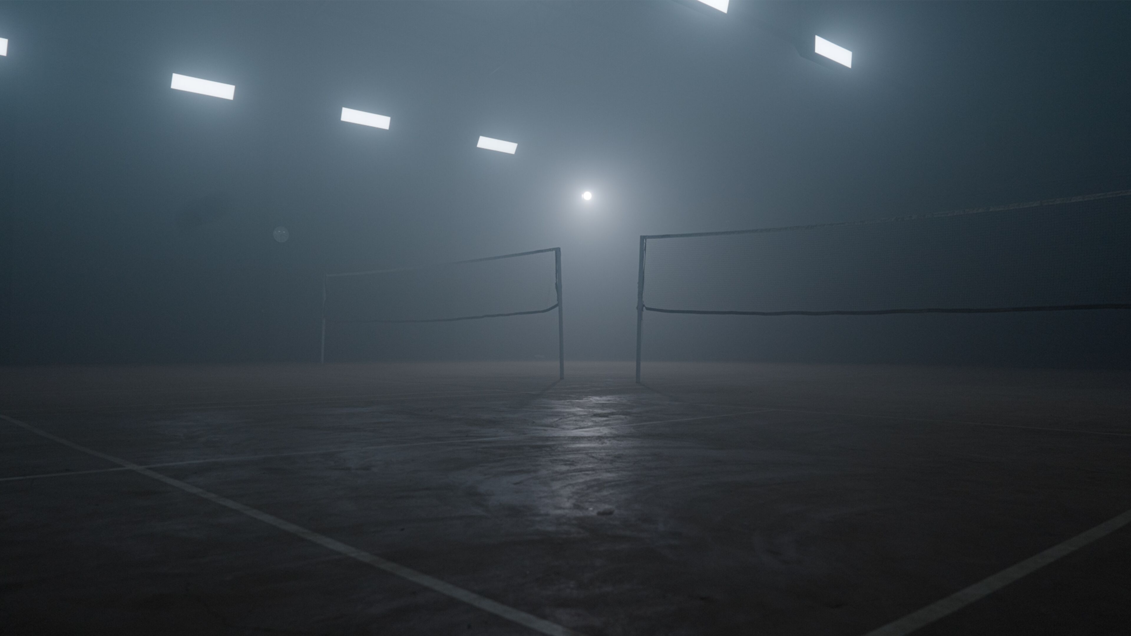 An indoor tennis court with a net, floodlights, and a foggy atmosphere.