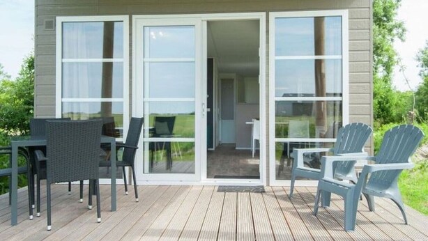 Una terraza de madera con una mesa y sillas, un patio con puerta corrediza y vista a la vegetación.