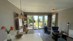 Una sala de estar moderna con comedor, grandes puertas correderas de vidrio que dan a un patio exterior y vistas a zonas verdes.