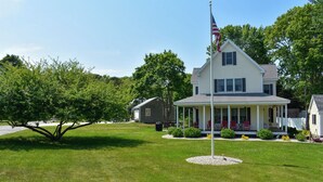 Une maison à deux étages avec un porche, un mât sur lequel flotte le drapeau américain, et une pelouse bien entretenue.