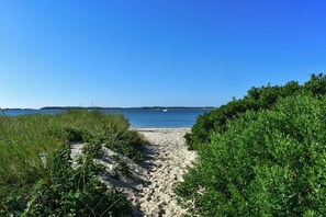 Een zandpad langs het strand dat uitkomt bij een rustige zee onder een heldere lucht.