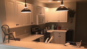 Cocina moderna con armarios blancos, una isla central con taburetes y luminarias colgantes.