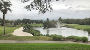 Un campo de golf con un estanque, una fuente de agua y un sendero.