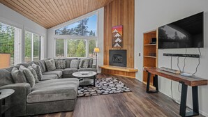 Ein modernes Wohnzimmer mit einem Ecksofa, einem Kamin, einem an der Wand befestigten Fernseher und einer Holzbalkendecke.