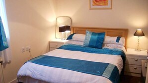 Ein ordentlich bezogenes Bett mit blauer und weißer Bettdecke, zwei Nachttischlampen und einem an der Wand befestigten Spiegel.