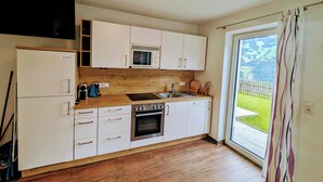 Cozinha moderna com armários brancos, micro-ondas embutido, fogão e uma janela grande com vista para uma paisagem verde.
