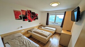 Quarto compacto com duas camas, televisão e janela com vista.