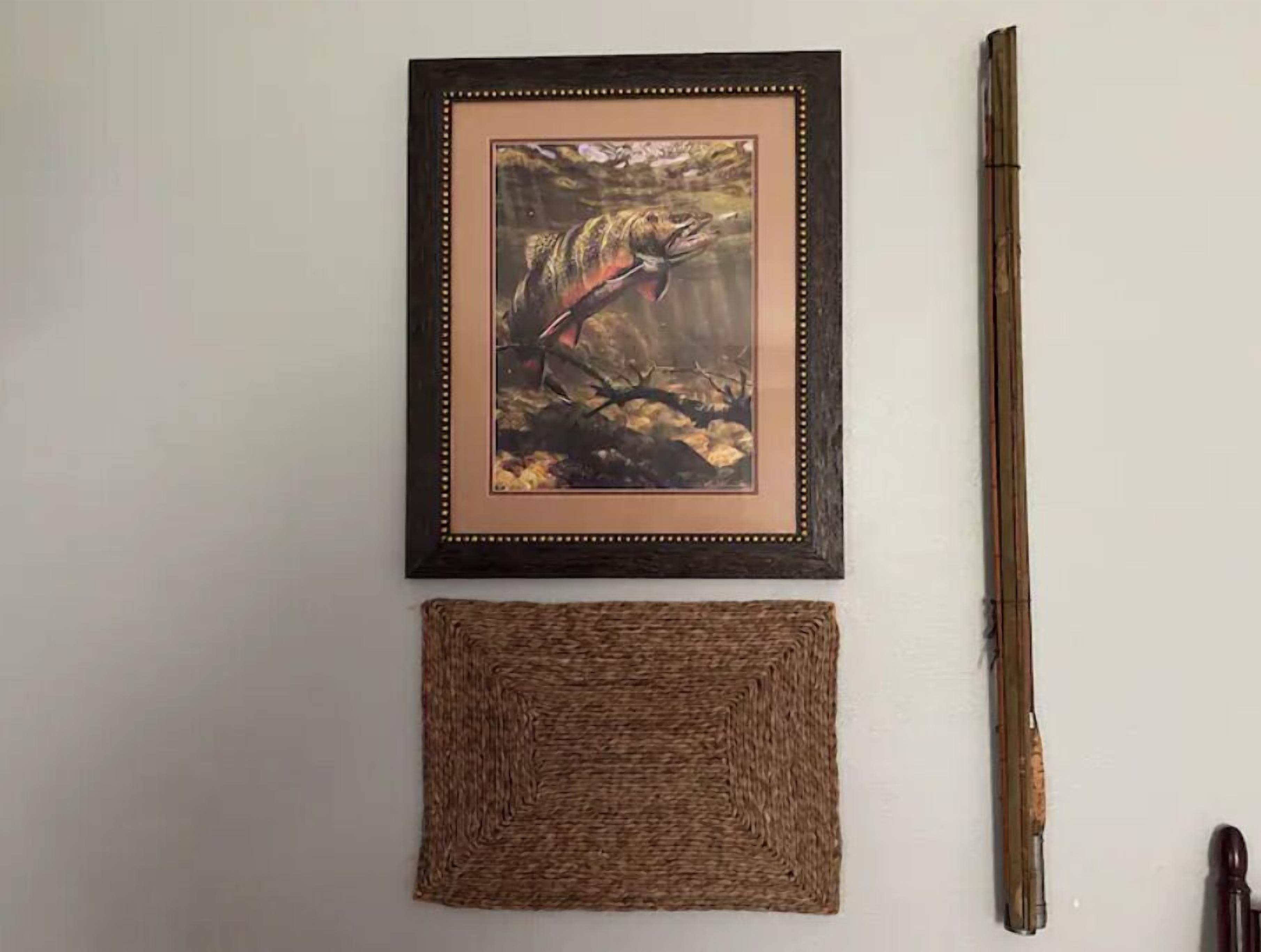 Een lijst met een schilderij van een vogel op een tak, een geweven onderzetter en een houten voorwerp.