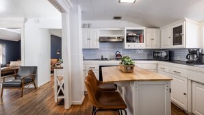 A modern kitchen with white cabinetry, a wooden island, and a dining area with leather chairs.