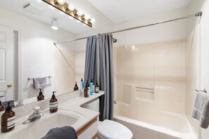 A modern bathroom with a bathtub, shower, and toilet. There are toiletries on the counter and a towel rack.