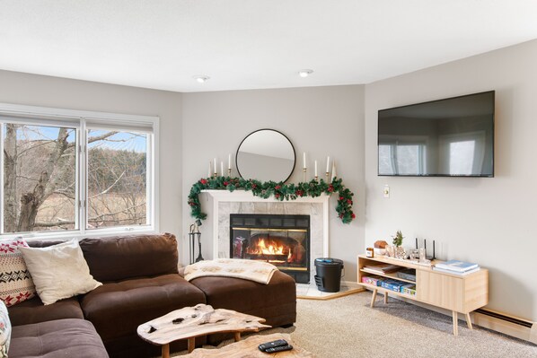 A living room with a fireplace, a sofa, a coffee table, and a TV mounted on the wall.