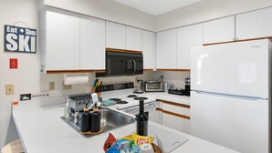 A modern kitchen with white cabinets, a stainless steel sink, a refrigerator, and a microwave. There is a sign on the wall that reads "Eat Sleep Ski". - Mount Snow Condo: 4 min Walk to Sundance Lift (High Speed - 6 Seat) (Dover)
