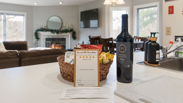 A kitchen counter with a bottle of Cabernet Sauvignon, a feedback card, and a basket of fruits. - Mount Snow Condo: 4 min Walk to Sundance Lift (High Speed - 6 Seat) (Dover)