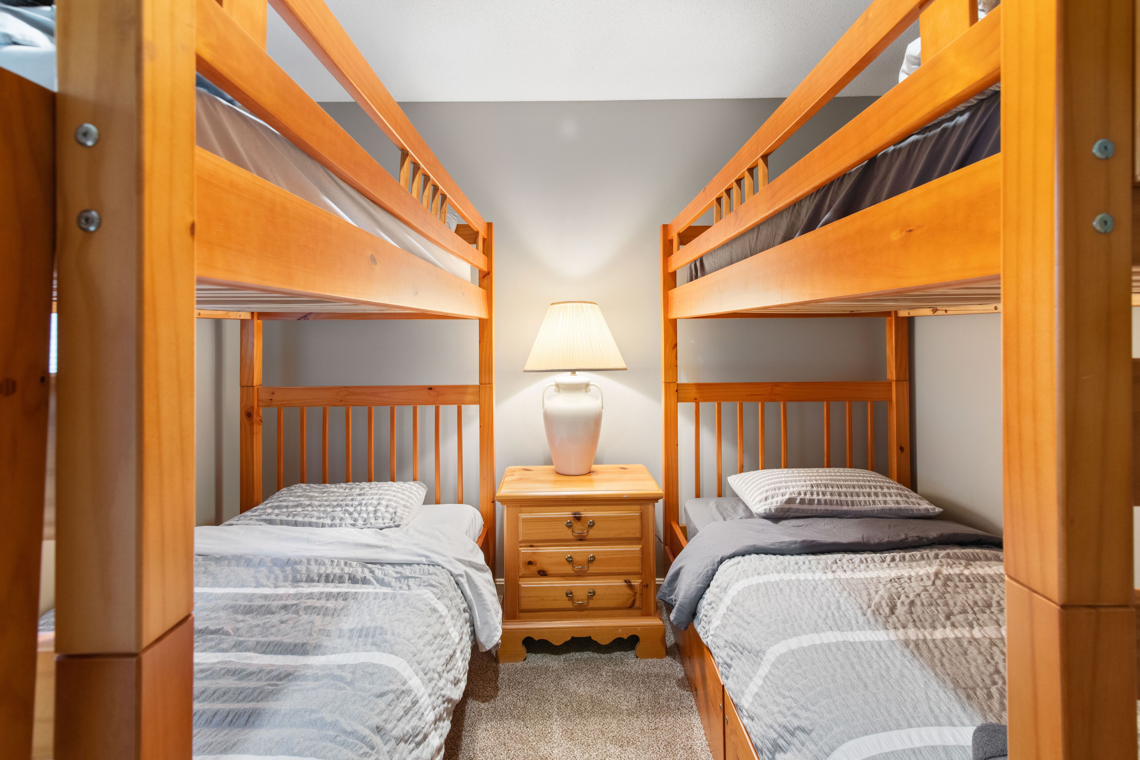 Une chambre avec un lit superposé, une table de chevet et une lampe placés entre les lits.