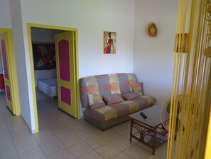 Un salon avec un canapé, une petite table, un ventilateur et un tableau accroché au mur.