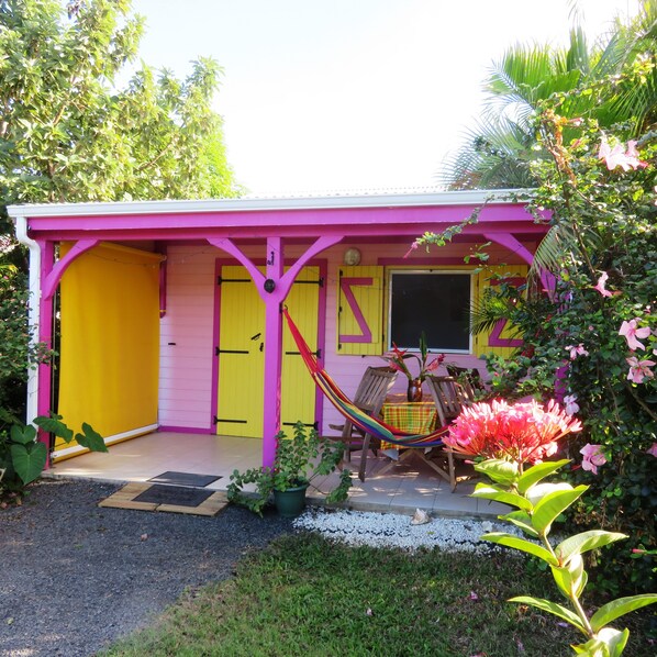 Une maison à la façade rose et jaune, avec un hamac et un petit espace patio.