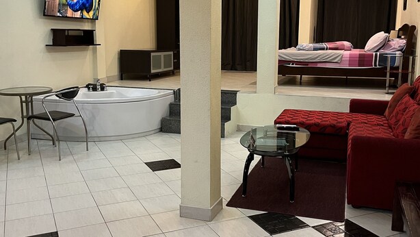 A hotel room with a bed, a red sofa, a glass table, a TV, a bathtub, and a small table with chairs. - Freeway Pattay make you feel as home (Pattaya)