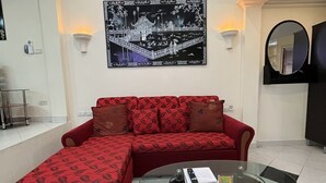 A living room with a red sectional sofa, a glass coffee table, a black and white artwork on the wall, and a round mirror. - Freeway Pattay make you feel as home (Pattaya)