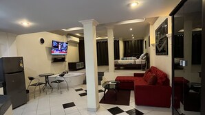 A modern living room with a red sofa, a dining area with a table and chairs, a kitchen area with a refrigerator, and a TV mounted on the wall. - Freeway Pattay make you feel as home (Pattaya)