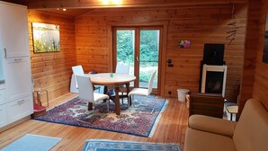 Ein gemütliches Blockhaus-Interieur mit einem Holzesstisch, weißen Stühlen, einer Couch und einem Kamin.