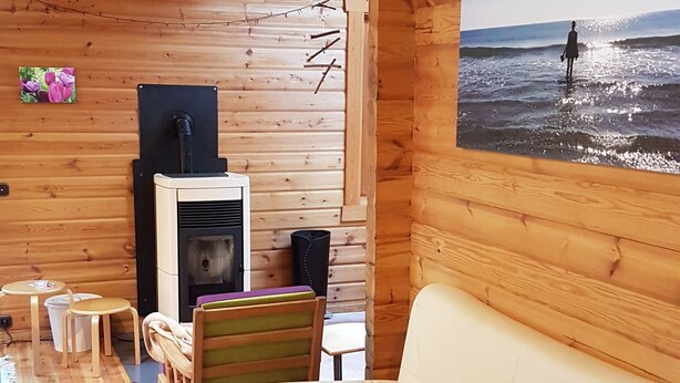 Ein gemütliches Blockhaushaus-Interieur mit einem beigen Sofa, Holzwänden, einem Kamin und Blick aufs Meer.