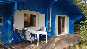 Eine blaue Holzhütte mit einer Holzterrasse, einem Tisch und zwei Stühlen.