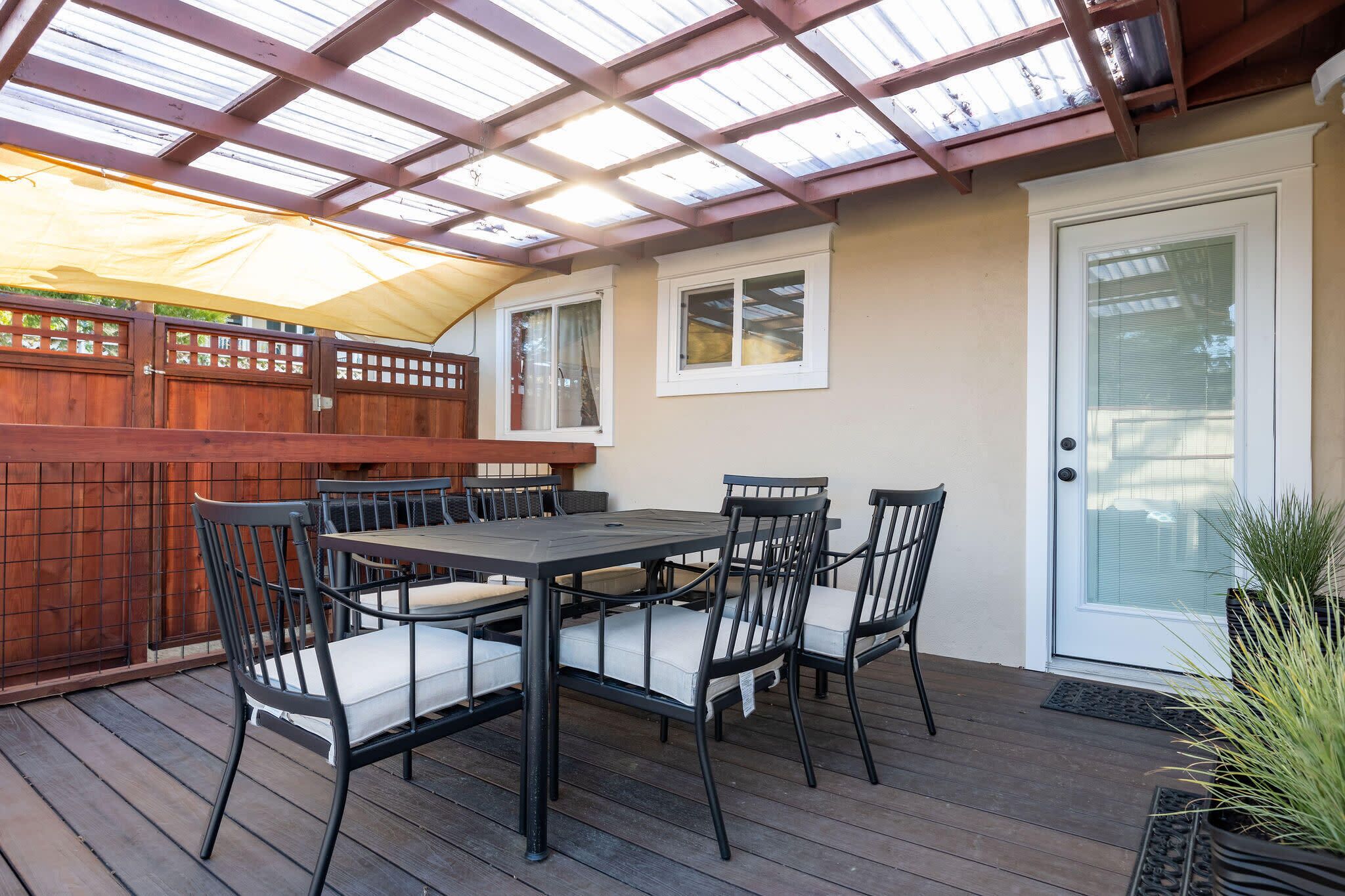 Een overdekt terras met een houten terras, een tafel met stoelen en een deur met een ruit.